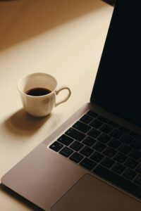 A minimalist workspace featuring a cup of coffee next to a laptop on a light-colored desk.